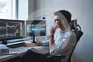 Busy working day. Side view of successful trader or businessman in formal wear and eyeglasses working with charts and