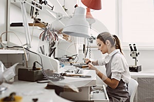Busy working. Side view of young female jeweler working on a new jewelry product at her workbench. Jewelry making