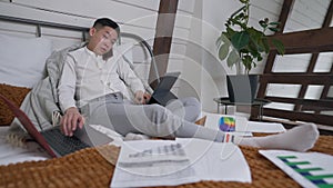 Busy young Asian man talking on the phone messaging on laptop and surfing Internet on tablet in home office. Overworking