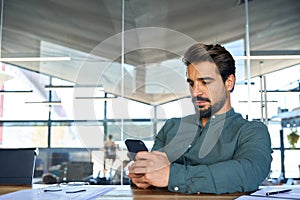 Busy young Latin business man using mobile cell phone at work in office.