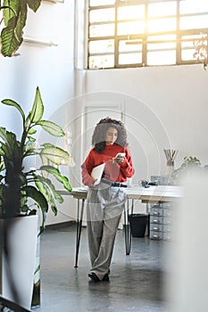 Busy young latin business woman using phone standing in office.