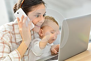 Busy young woman on laptop holding her baby