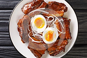 Buta no kakuni is a classic Japanese dish of braised pork belly with boiled eggs close up in the plate. Horizontal top view
