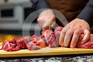 A butcher in an apron in the kitchen cuts pork on a wooden board. Steak.