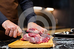 A butcher in an apron in the kitchen cuts pork on a wooden board. Steak.