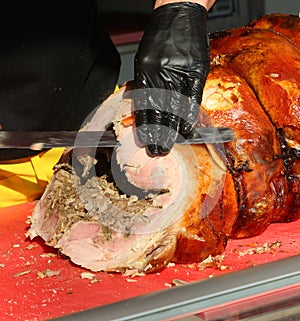 butcher with black glove cuts slices of porchetta a pork salume photo