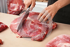Butcher cutting fresh raw meat on counter in shop