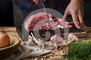 Butcher cutting pork on wooden board on a wooden table on the dark background