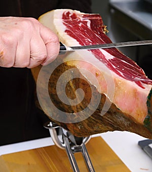 Butcher cutting a slice of a tasty piece of bone ham