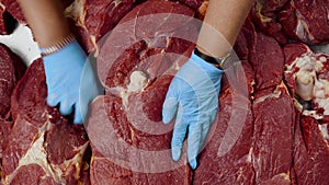 Butcher in gloves puts on display beef steak on the market window close-up.