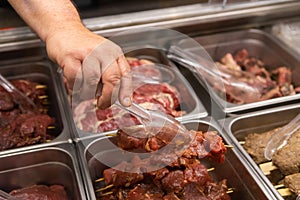 Butcher hand holding fresh meat skewer.