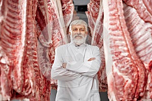 Butcher posing, standing between rows of pork carcasses.
