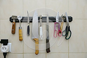 butcher's knives scisors and other kitchen utensils hanging on a rack on wall, restaurant kitchen