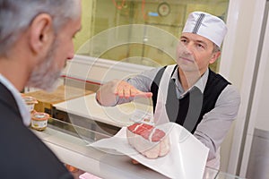 Butcher serving joint meat to customer