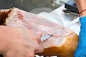 Butcher Slicing with Long Knife Smoked Baked Pork Ham from Leg at Market. Close up of Meat Texture