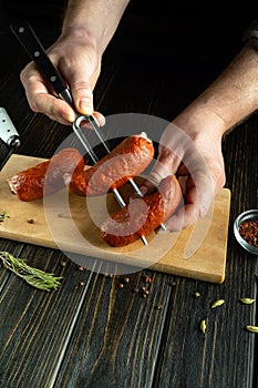 A butcher threads sausages onto a fork for grilling. Concept of cooking sausages on a barbecue kitchen table. Place for