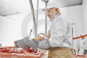 Butcher working with electric knife and cutting pork.