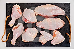 Butchered carcass of raw chicken on a black cutting board on a white background