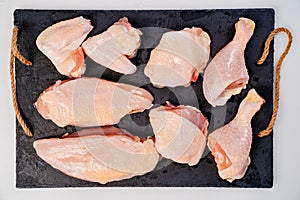Butchered carcass of raw chicken on a black cutting board on a white background
