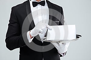 Butler in tuxedo and gloves holding blank card on tray