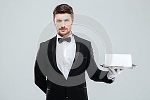 Butler in tuxedo and gloves holding tray with blank card
