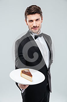 Butler in tuxedo holding piece of cake on plate