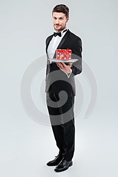 Butler in tuxedo standing and holding tray with gift box