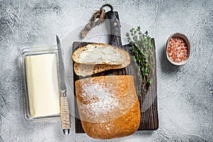 Butter block and sliced toasts of bread on a wooden board with herbs. White background. Top view