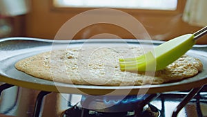 Butter brush spreads pancake on hot pan gas stove in kitchen. Slowmo closeup