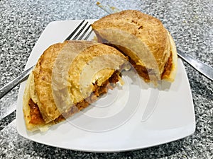 Butter chicken pie on white plate with fork and knife on grey table.