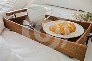 Butter cookies and coffee cup in wooden tray on comfortable bed