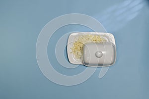Butter grated with fine shavings, in white ceramic oil with ajar lid, on a blue background in the center