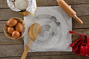 Butter paper, flour, rolling pin cookie cutter and eggs kept over a wooden table