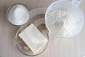 Butter on a plate and a glass of sugar and flour on a wooden table close up