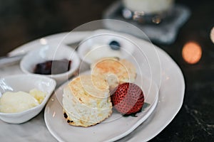 Butter scones served with jam and clotted cream with strawberries on white plate.Breakfast, Traditional English Afternoon Tea,