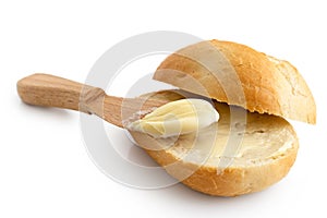 Butter spread on a cut crusty bread roll with a wooden knife iso