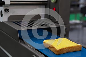 Butter spread on fresh bread slice in production line on the conveyor belt of automatic bread buttering machine at bakery factory