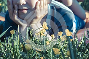 Buttercups and grass in the foreground. A blurred silhouette of a child lying on his stomach and supporting his head with his hand