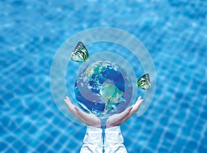 Butterfly drinking water from blue globe on hand. Saving water concept