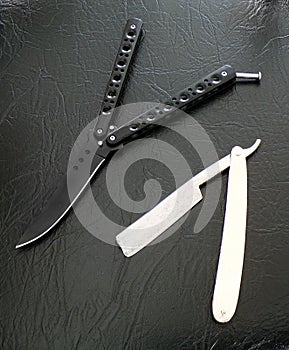 Butterfly knife and a manual razor on a black background. photo