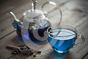 Butterfly pea blue tea in a glass cup on a wooden table, a teapot and dry leaves of clitoria trifoli