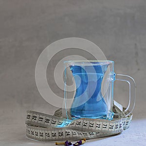 Butterfly pea flower blue tea in glass mug with silhouette like slim woman figure. With measuring tape around as drink helps to