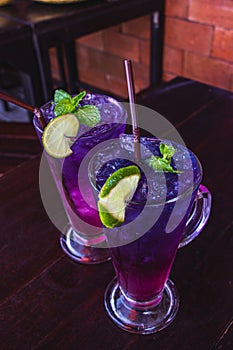 Butterfly pea juice with lemon in clear glass put on dark brown wooden table are thai herb drink for health and refreshing. Select