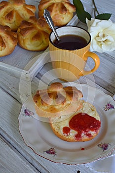Buttermilk dinner buns in flower form served with butter, knife, glass of milk and jam on wooden background. Fresh baked brioche.