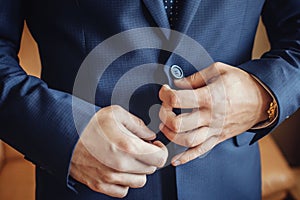 Buttoning a jacket hands close up. Stylish man in suit fastens buttons and straightens his jacket preparing to go out. Preparing