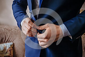 Buttoning a jacket hands close up. Stylish man in suit fastens buttons and straightens his jacket preparing to go out. Preparing