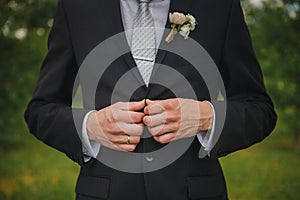 Buttoning a jacket hands close up. Stylish man in suit fastens buttons and straightens his jacket. Preparing for a wedding