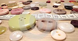 Buttons, needles, pins, spools and tailor`s tape on wooden desk , close up. Fashion designer desk with equipment, tailoring and