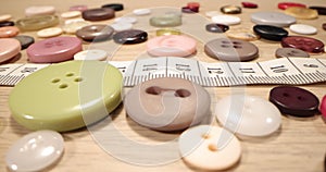 Buttons, needles, pins, spools and tailor`s tape on wooden desk , close up. Fashion designer desk with equipment, tailoring and