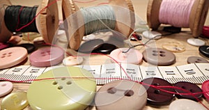 Buttons, needles, pins, spools and tailor`s tape on wooden desk , close up. Fashion designer desk with equipment, tailoring and